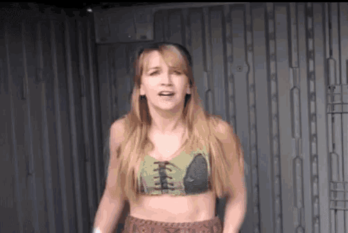 a woman in a crop top and shorts is standing in front of a chain link wall .