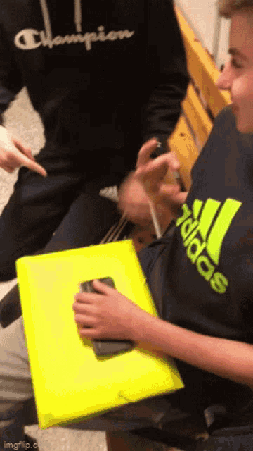 a boy wearing an adidas shirt is holding a cell phone