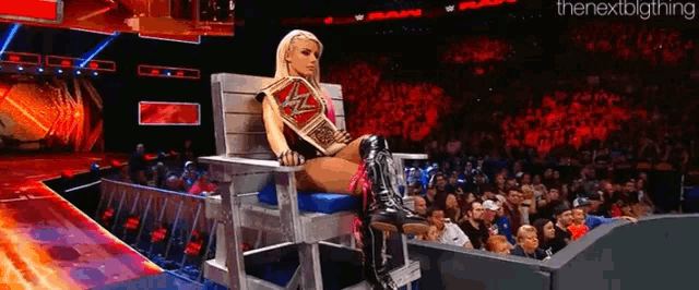 a woman is sitting in a chair in front of a crowd holding a wrestling championship belt .