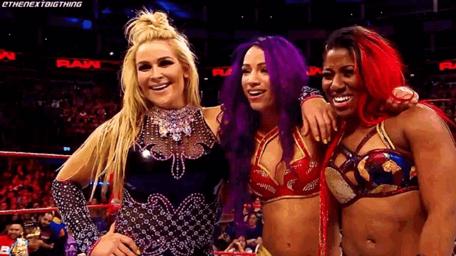 three female wrestlers are posing for a picture together in a ring .