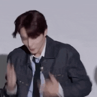 a man in a denim jacket and tie is dancing in front of a white wall .