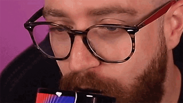 a man with glasses and a beard is drinking from a bottle .