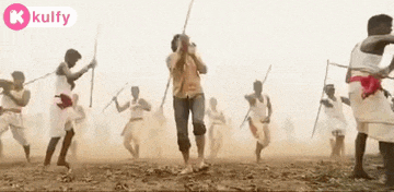a group of men are dancing in the dirt with sticks in their hands .