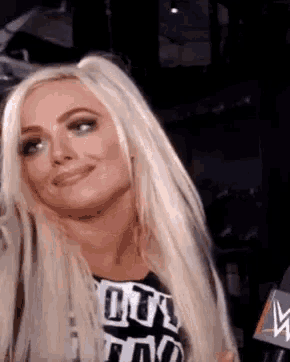 a woman with blonde hair is smiling and wearing a black and white shirt with the letter w on it .