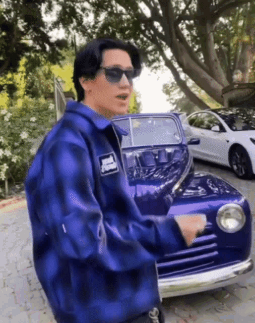 a man wearing sunglasses and a blue plaid shirt is standing next to a purple car
