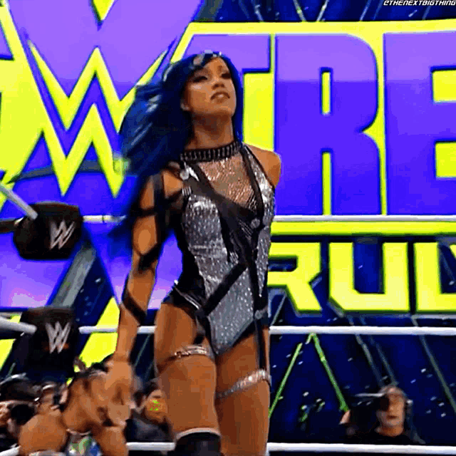 a woman with blue hair is standing in a wrestling ring in front of a sign that says w .