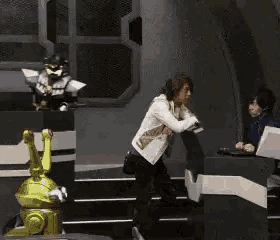 a woman is standing in front of a robot while a man sits at a desk .