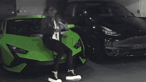 a man in a black jacket is sitting on the hood of a green car .