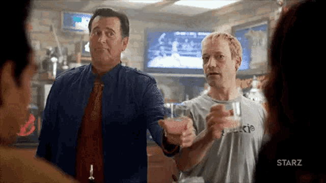 two men are standing next to each other in a bar holding glasses of alcohol .