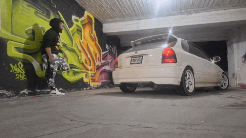 a man standing next to a white car with a license plate that says tmc5208