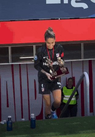 a female soccer player holds a trophy in front of a sign that says herbalife