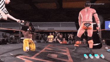 a wrestler is kneeling down in a ring while a referee holds a rope