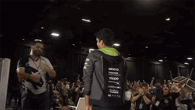 two men shake hands in front of a crowd with one wearing a hoodie that says ' ecg ' on the sleeve