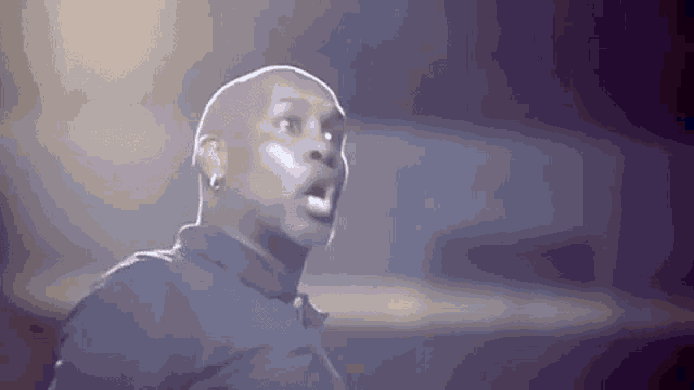 a bald man in a black shirt is making a funny face in a dark room .
