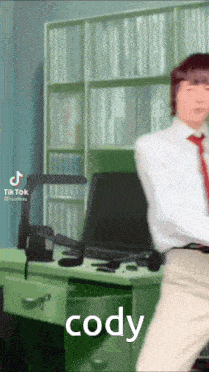 a man in a white shirt and red tie is dancing in front of a desk with the name cody written on it