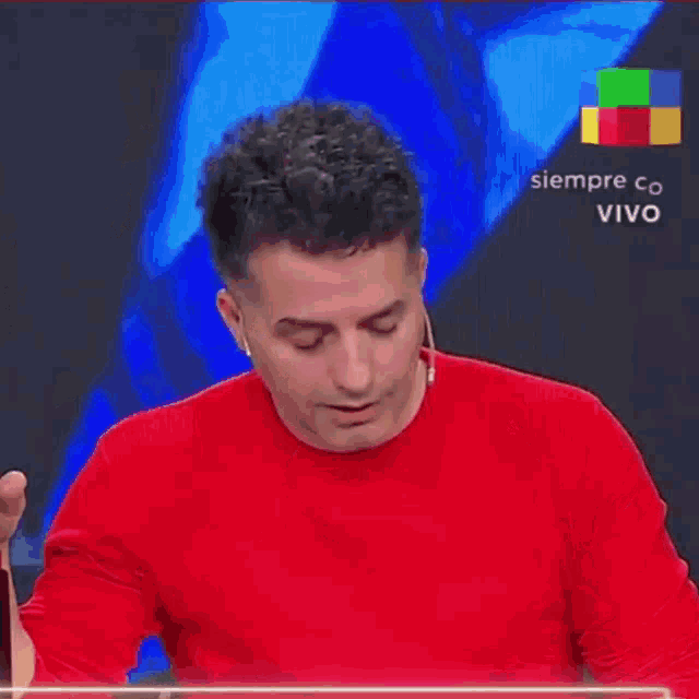 a man in a red shirt is laughing in front of a sign that says siempre con v vivo