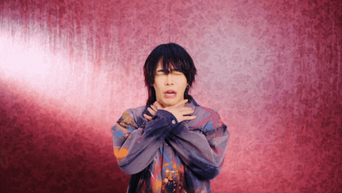 a man covering his mouth with his hands in front of a red wall