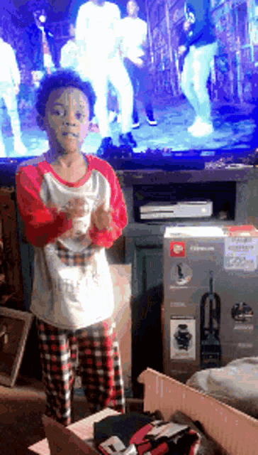 a young boy in pajamas is standing in front of a tv screen
