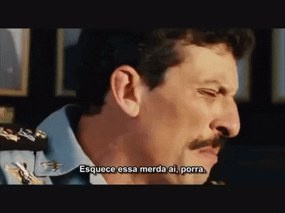 a man with a mustache and a blue shirt is talking in a movie .