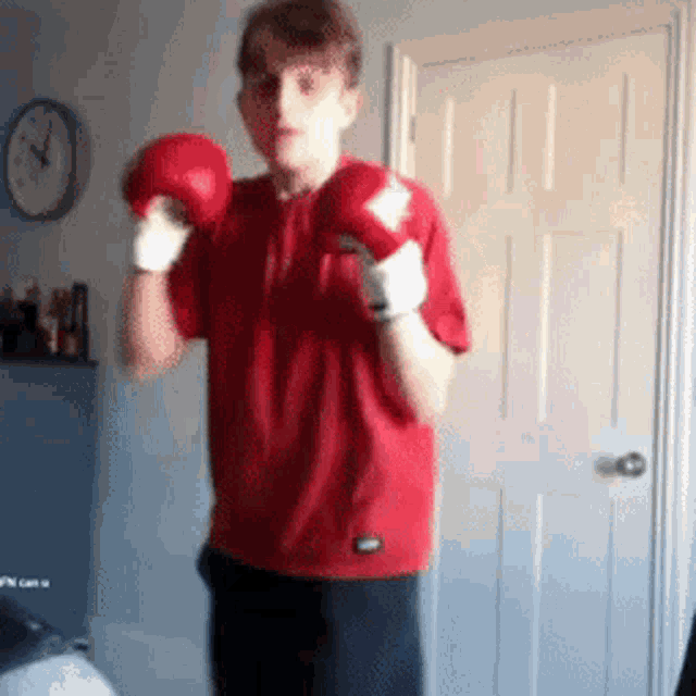 a boy in a red shirt is wearing boxing gloves in front of a clock