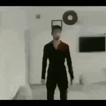 a man in a black jumpsuit is standing in a living room with a donut on the wall .