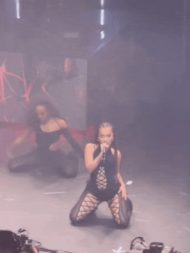 a woman is singing into a microphone while kneeling down