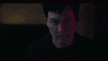 a man is holding a gun to his head and looking at the camera .