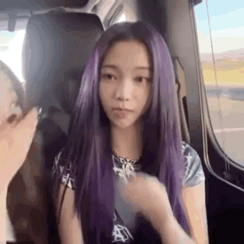 a woman with purple hair is sitting in a car with a person .
