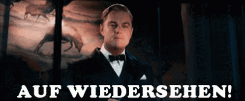 a man in a tuxedo is standing in front of a sign that reads auf wiedersehen