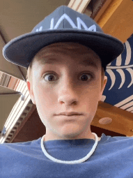 a young man wearing a hat and a necklace makes a funny face