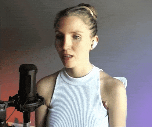a woman in a white tank top singing into a black microphone