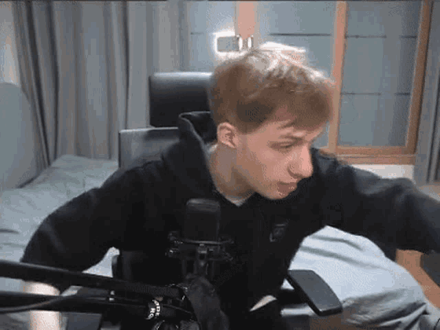a young man is sitting in a chair in front of a microphone in a bedroom .
