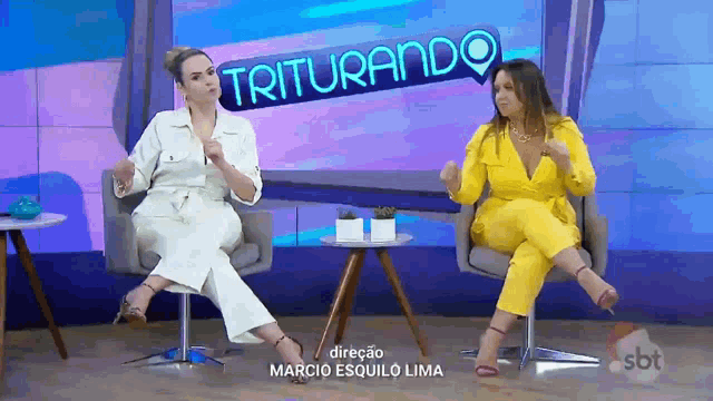 two women are sitting in front of a sign that says " triturando "