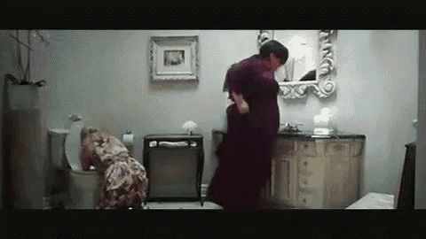 a woman is sitting on a toilet in a bathroom while a man is standing next to her .
