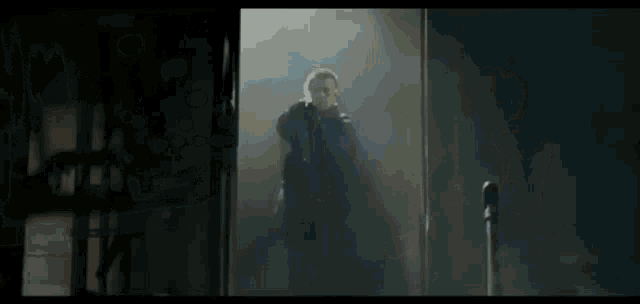 a man in a black jacket is standing in a dark room holding a gun .