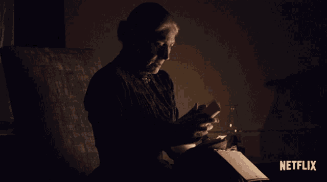 a woman sits in a dark room reading a book with a netflix logo on the bottom