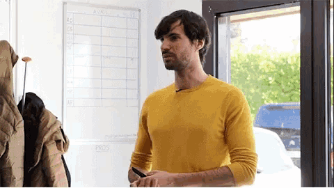 a man in a yellow sweater stands in front of a white board that says " pros "