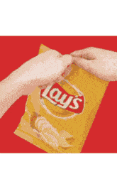 a person is opening a bag of lays chips on a red background