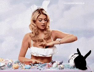 a woman in bunny ears is sitting at a table with easter eggs and a bunny rabbit .