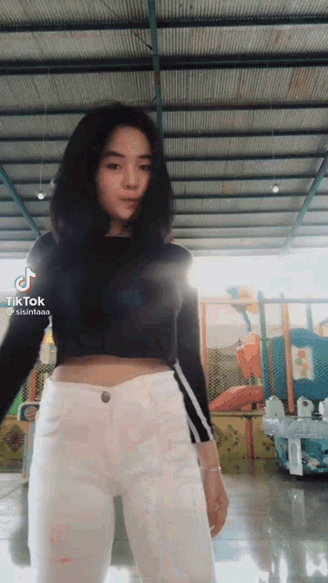 a girl in a black crop top and white pants is standing in a playground .