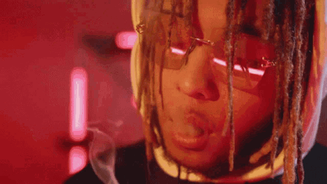 a man with dreadlocks and sunglasses is smoking a cigarette in a red room .
