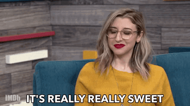 a woman in a yellow sweater is sitting on a blue couch and says it 's really really sweet