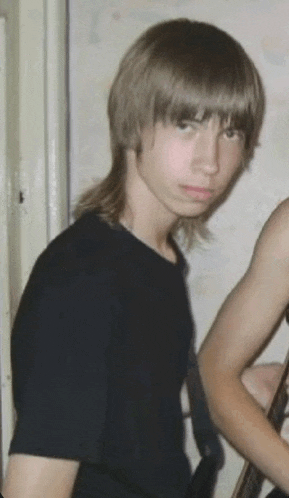 a young man with long hair is wearing a black shirt and standing next to another man .