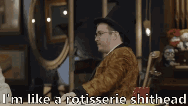 a man in a top hat is sitting in a chair with the words i 'm like a rotisserie shithead below him