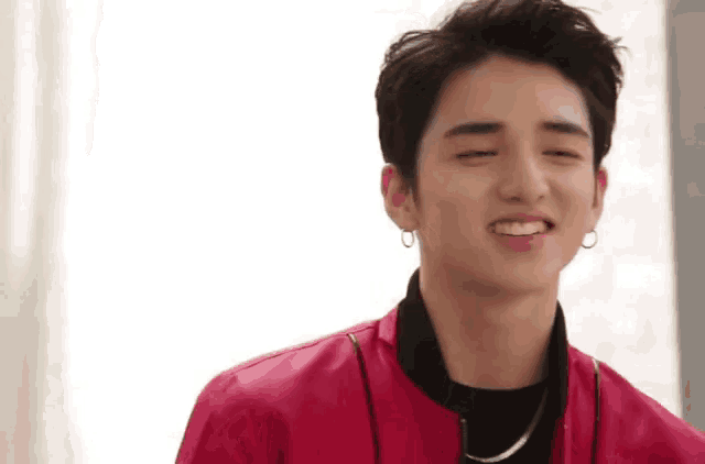 a young man wearing a red jacket and earrings smiles