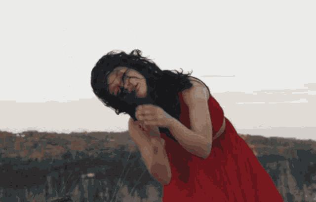 a woman in a red dress is standing in a field with her hair blowing in the wind