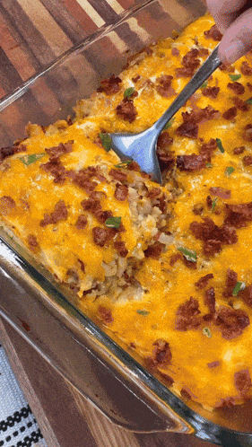 a glass casserole dish filled with rice cheese and bacon with a spoon in it