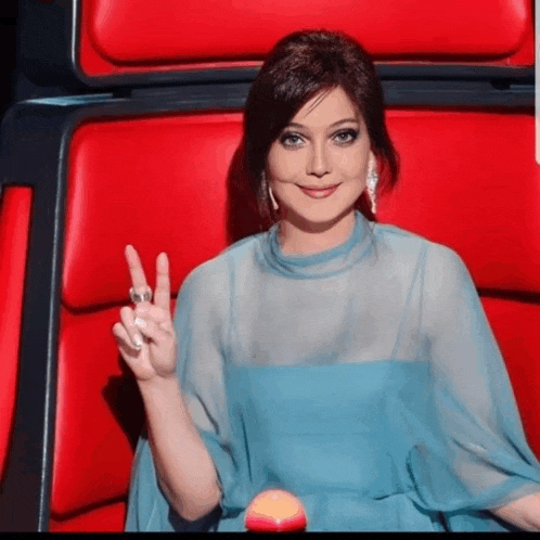 a woman in a blue dress is sitting in a red chair giving the peace sign