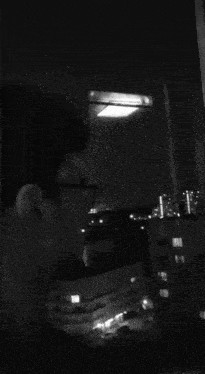 a black and white photo of a man looking out a window at night