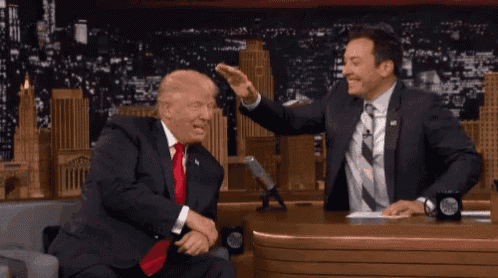 a man in a suit and tie touches the head of another man